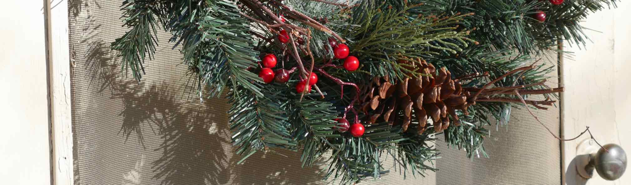 evergreen wreath with red berries and pine cone on door